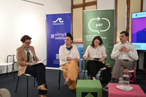 Panel z udziałem trzech osób i moderatorki. W tle widać roll-up organizatorów.
