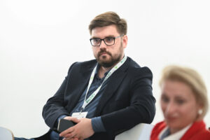 Uczestnik panelu przysłuchuje się rozmowie podczas panelu. Za nim biała ściana. 